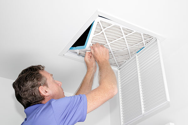 Stock Photo-Air Duct Cleaning -603 Chimney & Dryer Vent Inc.- Manchester NH Man opening his homes air conditioning air duct and looking into it and changing filter