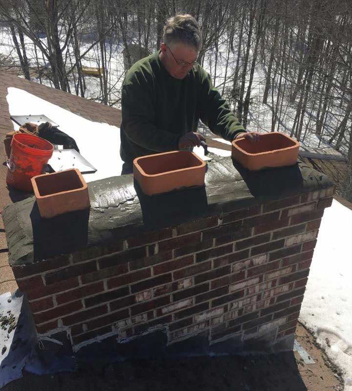 Man working on chimney crown and chase. Three chimney flues shown