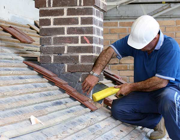 Stock Photo- Flashing Repair-603 Chimney & Dryer Vent Inc.- Manchester NH man in white hard hat kneeling at base of chimney to work on metal flashing