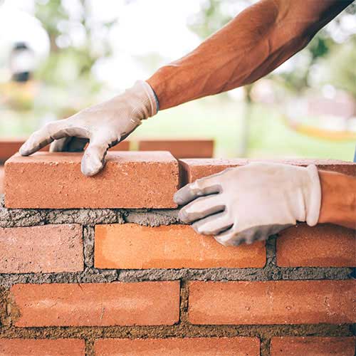 man wearing white gloves putting bricks in place with fresh mortar 