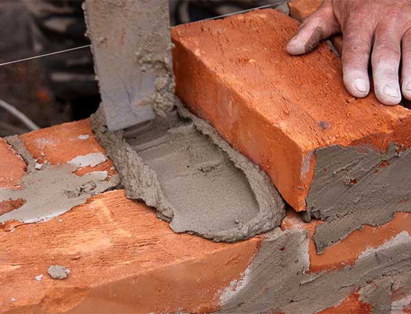 man's hand touching the top of bricks he is working on adding mortar to